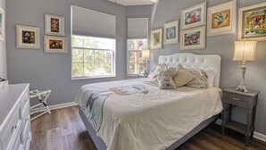 Een slaapkamer met een groot bed, een dressoir, een nachtkastje en een raam met jaloezieën.