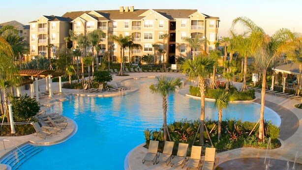 Een resort met een groot centraal zwembad, meerdere loungegedeeltes en een meerhoog gebouw met balkons.