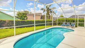A covered swimming pool with a clear blue water, surrounded by a white frame and a green hedge. - Kay's Southern Dunes Vacation Home (Haines City)