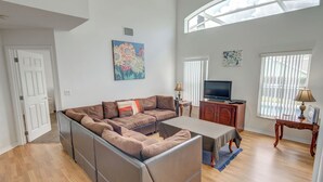 A spacious living room with a sectional sofa, a television, and a dining table. - Kay's Southern Dunes Vacation Home (Haines City)