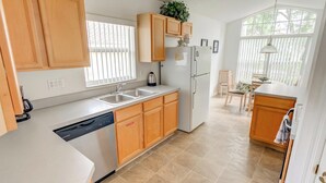 A modern kitchen with wooden cabinets, a dishwasher, a refrigerator, and a window with blinds. - Kay's Southern Dunes Vacation Home (Haines City)
