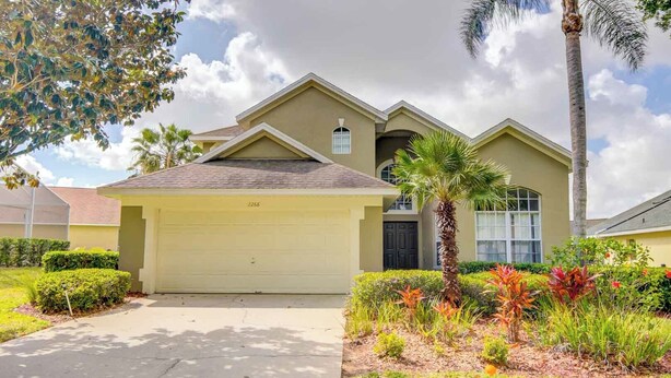 A two-story house with a garage, surrounded by well-maintained landscaping and a palm tree. - Kay's Southern Dunes Vacation Home (Haines City)