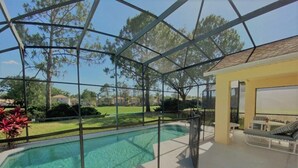 Ein überdachter Swimmingpool mit Glasveranda, eine Lounge mit Sofa und Tisch sowie Blick auf eine Wohngegend.