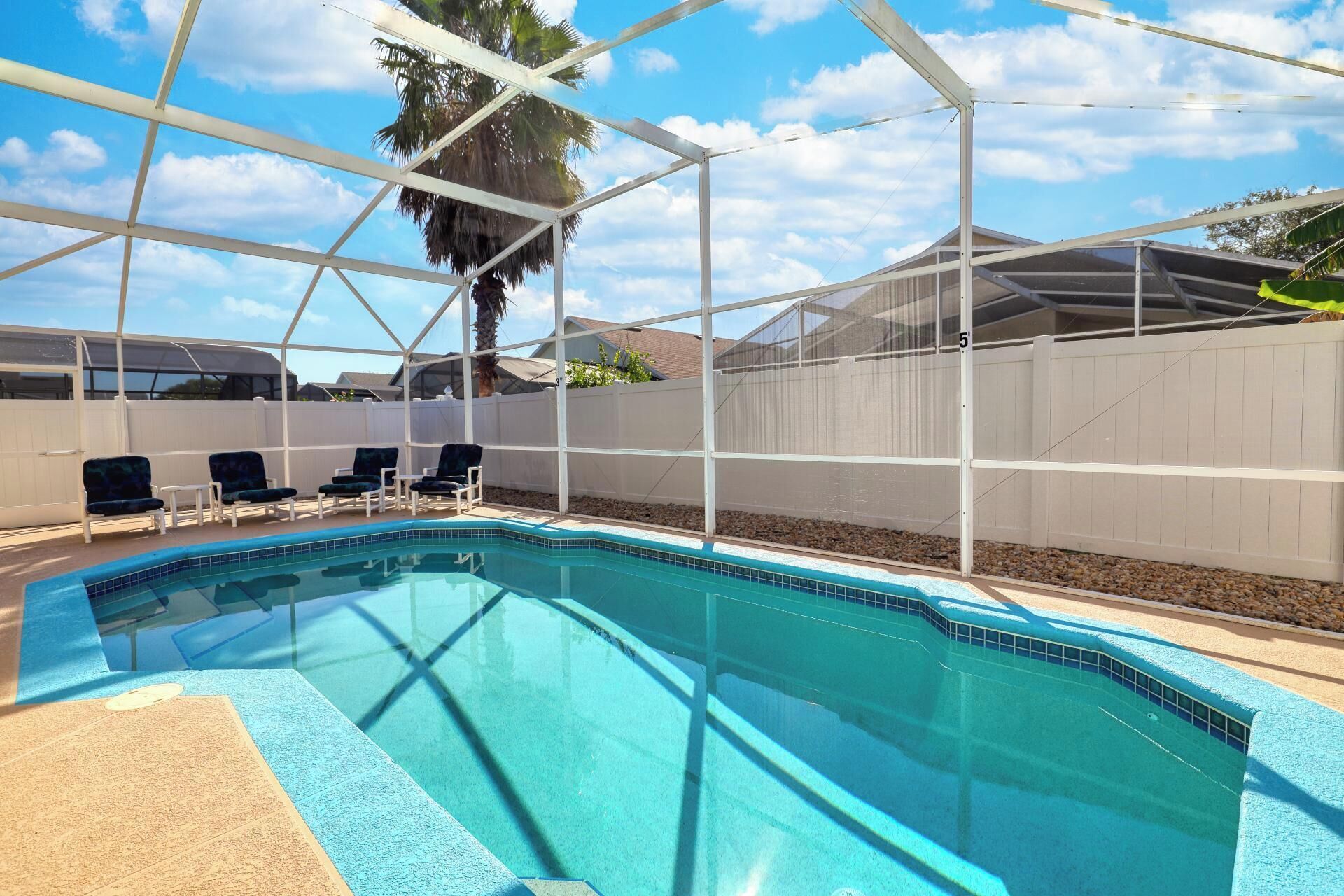 A swimming pool with a white fence and chairs.