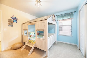 Casinha de brincadeira infantil com escada, decoração de parede com tema de praia e janela com cortinas estampadas.