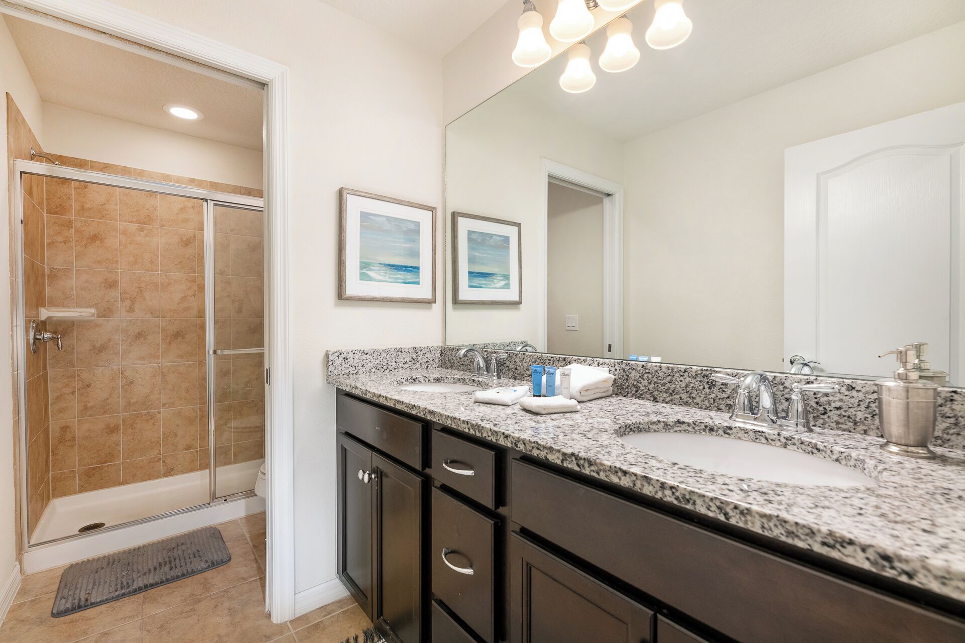 Une salle de bain avec une douche, deux tableaux encadrés au mur, un lavabo avec un miroir et un porte-serviettes.