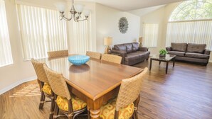 A spacious living room with a wooden dining table surrounded by wicker chairs, a leather sofa, and a coffee table. - Laguna Bay 007 (Kissimmee)