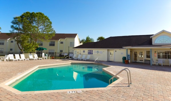A swimming pool with lounge chairs and a building with a tiled roof.