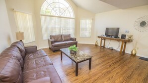 A spacious living room with a brown leather sofa, a wooden coffee table with a plant, and a television on a wooden stand. - Laguna Bay 007 (Kissimmee)