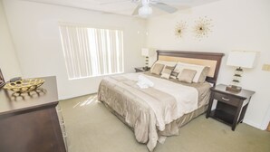 A bedroom with a large bed, two bedside tables, a nightstand, a dresser, a window with blinds, and a ceiling fan. - Laguna Bay 007 (Kissimmee)
