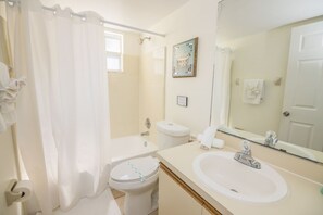 A bathroom with a shower curtain, toilet, sink, and a large mirror.