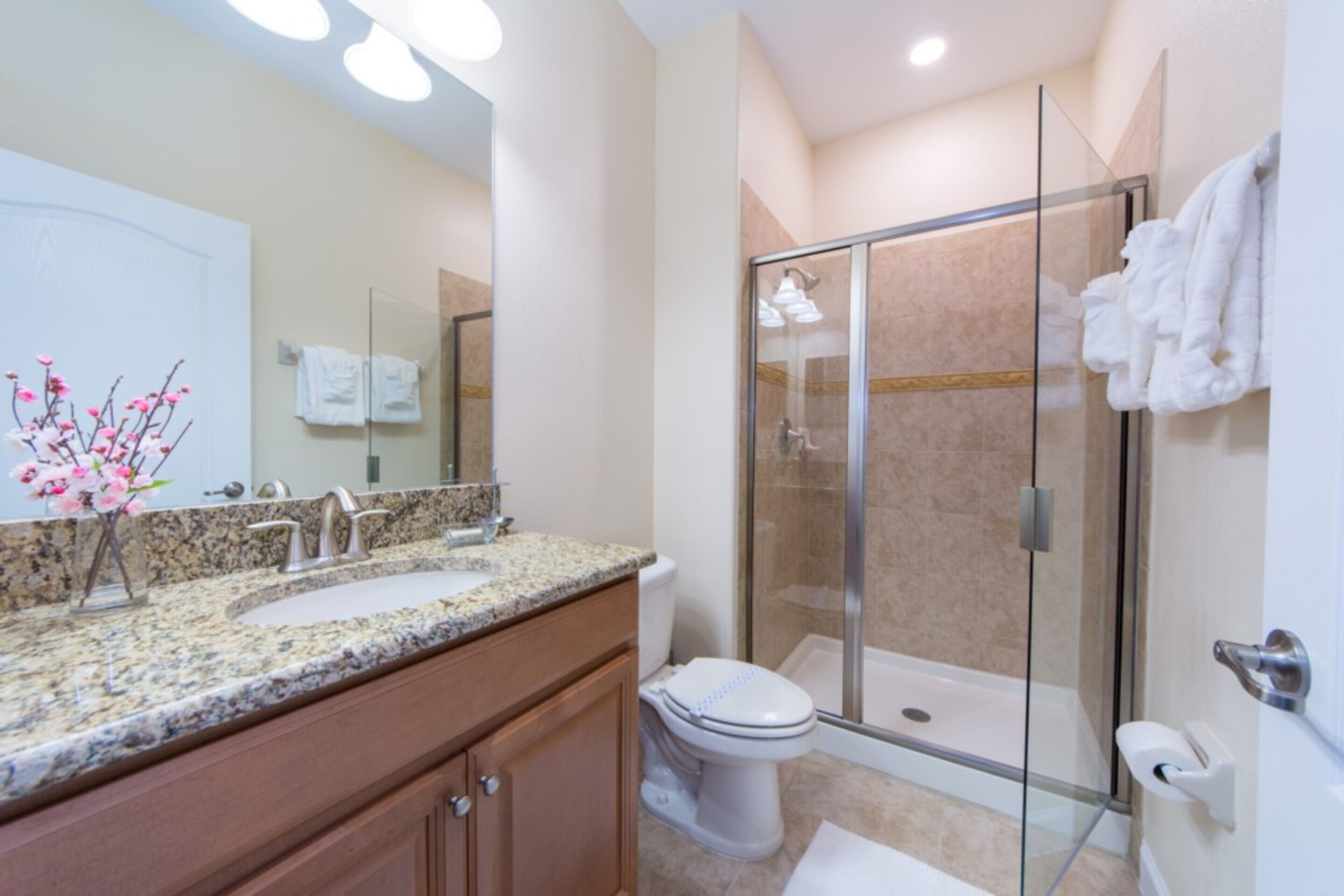 A modern bathroom with a granite countertop, two sinks, a toilet, and a glass-enclosed shower.