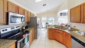 A modern kitchen with wooden cabinets, stainless steel appliances, granite countertops, and a view to the outdoor patio. - William's Lake Berkley Resort Vacation Home (Kissimmee)