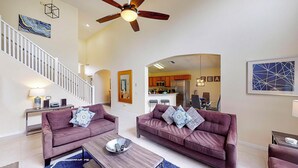A spacious living room with two sofas, a coffee table, and a ceiling fan. A staircase leads to an upper level. - William's Lake Berkley Resort Vacation Home (Kissimmee)