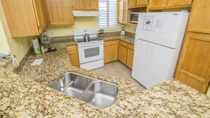 A kitchen with granite countertops, wooden cabinets, a stove, a refrigerator, and a double sink. - James' Runaway Beach Condo (Kissimmee)