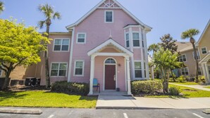 A pink two-story house with a central entrance, a small porch, and a garage. - James' Runaway Beach Condo (Kissimmee)