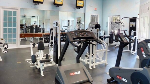 A gym with various exercise equipment, including treadmills and weight machines, and a large mirror wall. - Zacharias' Runaway Beach Condo (Kissimmee)