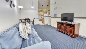 A living room with a sofa, TV stand, and dining area. - Zacharias' Runaway Beach Condo (Kissimmee)