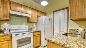 A kitchen with wooden cabinets, a white stove, a refrigerator, granite countertops, and a stainless steel sink. - Zacharias' Runaway Beach Condo (Kissimmee)