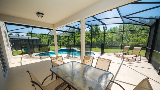 A covered patio with a glass table and chairs, a pool, and a view of a backyard. - Anastasia's Crystal Cove Vacation Home (Kissimmee)