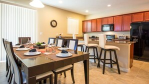 A modern kitchen with wooden cabinets, a central island, and a dining area with chairs and a table set for four. - Anastasia's Crystal Cove Vacation Home (Kissimmee)
