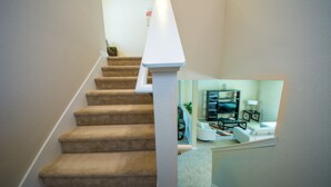 A carpeted staircase with a white handrail leading to a living area with a sofa, coffee table, and a television. - Anastasia's Crystal Cove Vacation Home (Kissimmee)