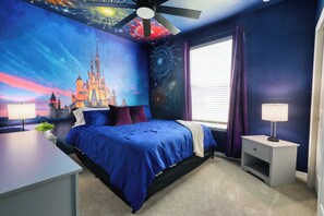 A bedroom with a large bed, a ceiling fan, a nightstand with a lamp, a window with purple curtains, and a mural of a castle on the wall.