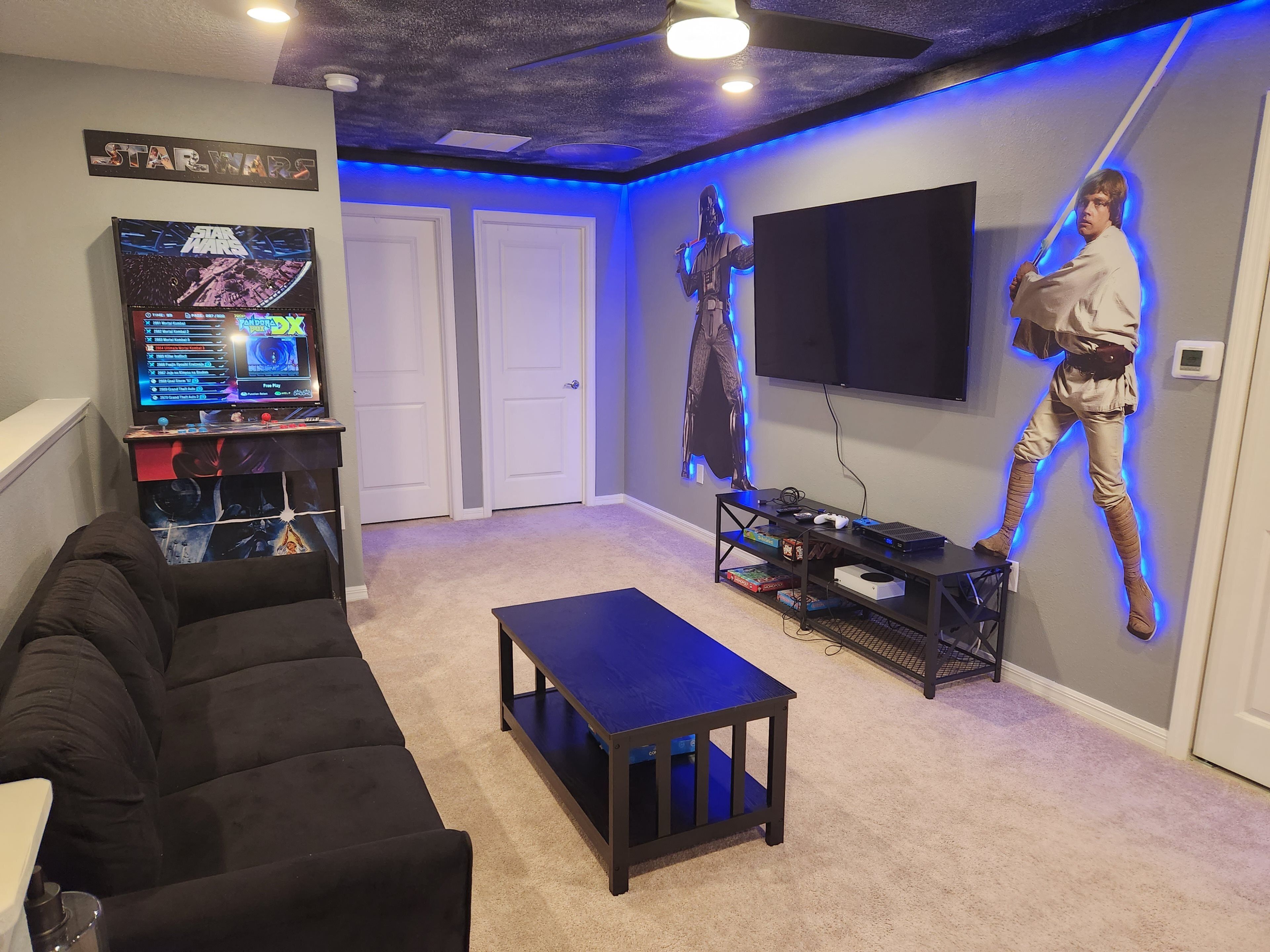 Una habitación con una decoración temática de Star Wars, que incluye una figura montada en la pared, una consola de videojuegos y un televisor grande.