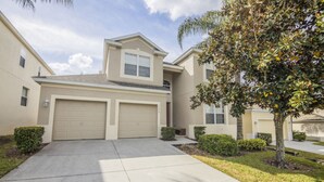 A two-story residential building with a garage, a small balcony, and a well-maintained lawn with a tree. - Bernard's Windsor Hills Resort Vacation Home (Kissimmee)