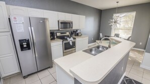 A modern kitchen with white cabinets, stainless steel appliances, a granite countertop, and a black and white rug. - Bernard's Windsor Hills Resort Vacation Home (Kissimmee)