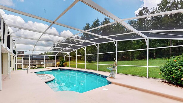 A covered swimming pool with a view of a backyard and a house.