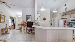 A spacious kitchen with a central island, white cabinetry, and a microwave. There are decorative items on the shelves and a clock on the wall.