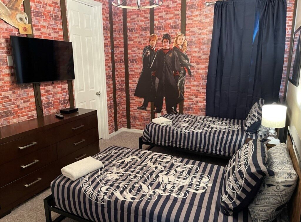 A bedroom with two beds, a TV, a dresser, and a brick wall mural.