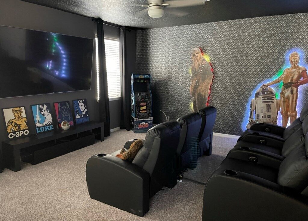 A home theater room with a large flat-screen TV, reclining chairs, and Star Wars-themed decorations.