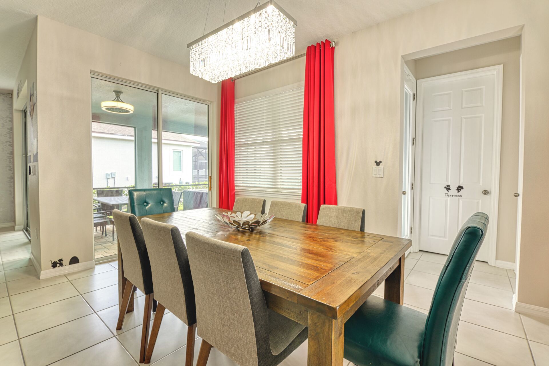 A dining area with a wooden table, six chairs, red curtains, and a chandelier.