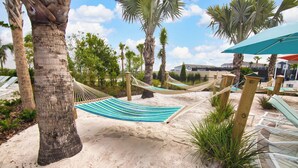 A hammock set up between palm trees on a sandy beach, with a view of a residential area in the background. - A Touch of Blue at Windsor Island Resort (Davenport)