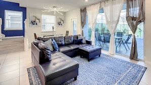 A modern living room with a sectional sofa, a chandelier, and a view of the outdoor patio. - A Touch of Blue at Windsor Island Resort (Davenport)