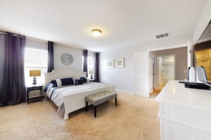A bedroom with a bed, bedside table, lamp, and a bench. There is a door leading to another room and a white dresser. - Richard's Solterra Vacation Home (Davenport)