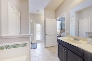 A bathroom with a large mirror, a sink, and a toilet. There is a door leading to another room. - Richard's Solterra Vacation Home (Davenport)