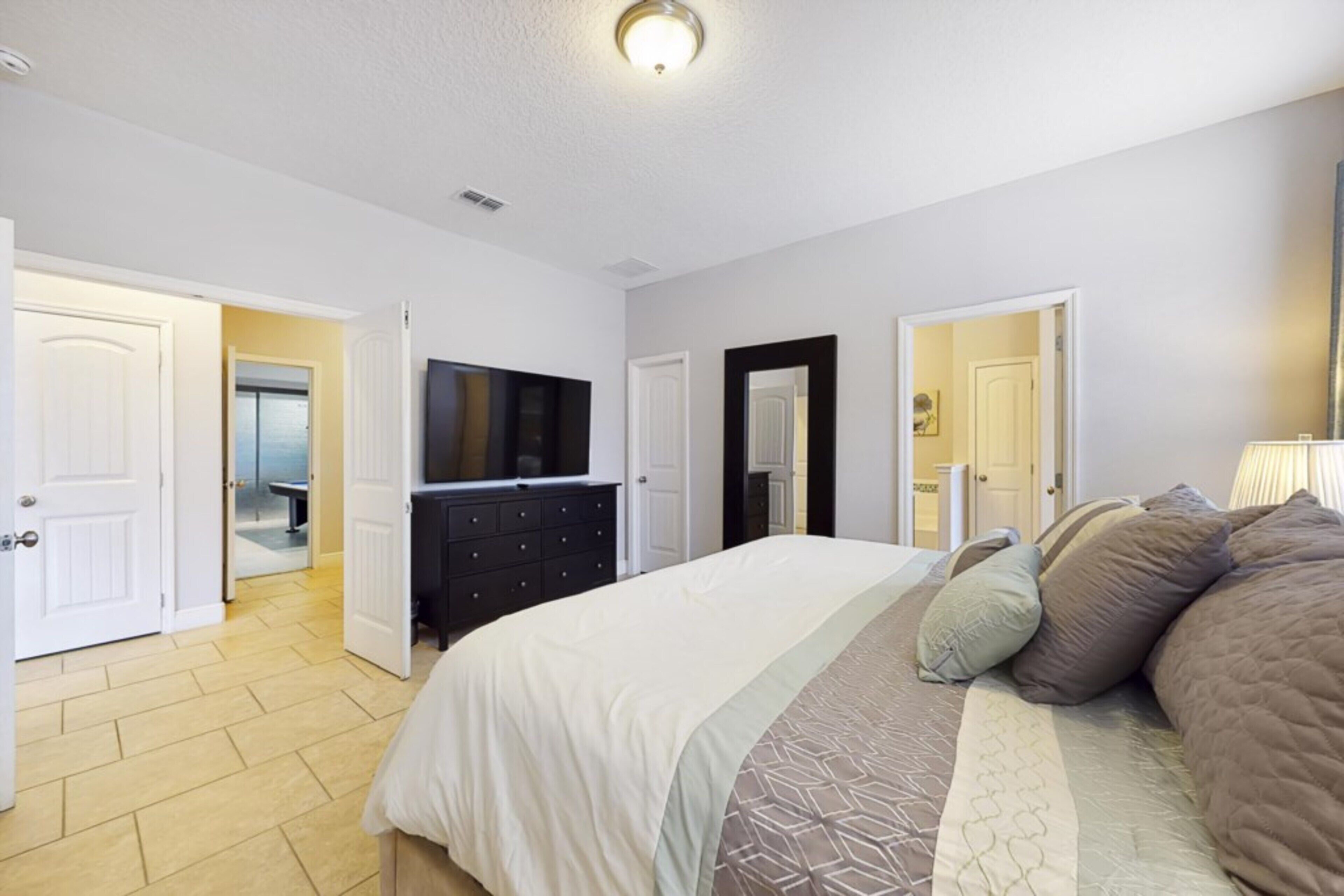 A bedroom with a bed, dresser, and television. There are doors leading to other rooms.