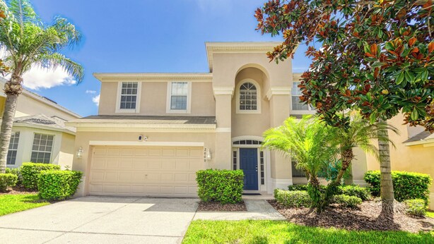 A two-story house with a garage, a central arched entrance, and a well-maintained lawn. - Christopher's Windsor Hills Home (Kissimmee)