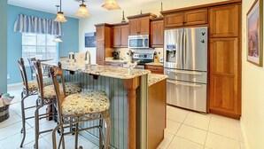 A kitchen with wooden cabinets, stainless steel appliances, a marble countertop, and pendant lighting. - Comrow Castle Magical Getaway (Kissimmee)