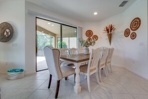 A dining area with a wooden table and white upholstered chairs, a vase with flowers, and decorative wall art. - Beautiful Providence Vacation Home (Davenport)