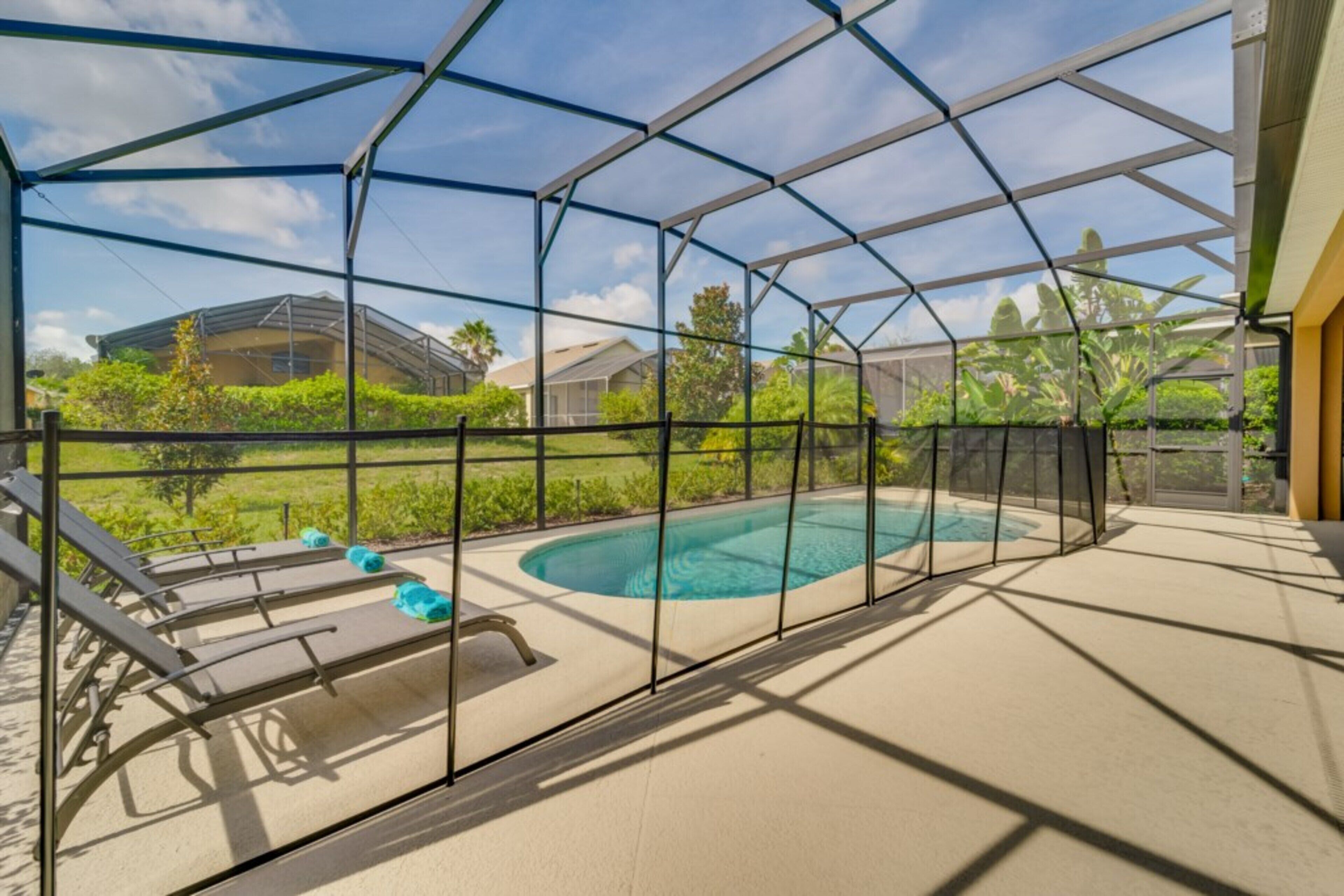 A covered outdoor swimming pool with lounge chairs and a view of houses and greenery.