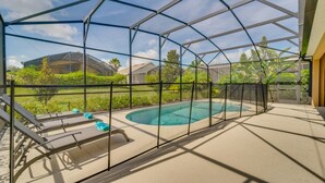 A covered outdoor swimming pool with lounge chairs and a view of houses and greenery. - Beautiful Providence Vacation Home (Davenport)