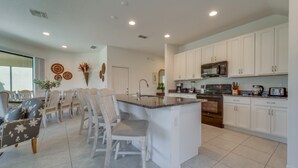 A modern kitchen with white cabinets, a central island, and a dining area with chairs and a table. - Beautiful Providence Vacation Home (Davenport)