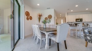 A dining area with a wooden table and white upholstered chairs, a kitchen with white cabinets, and decorative wall art. - Beautiful Providence Vacation Home (Davenport)