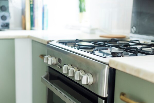 Una cocina con estufa, horno de acero inoxidable y una ventana con libros al fondo.