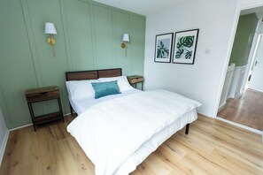 Une chambre avec un plancher en bois, un lit avec une literie blanche, deux tables de chevet et des lampes fixées au mur.