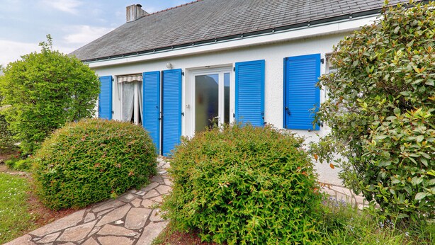 A white building with blue shutters, a stone pathway, and green bushes.